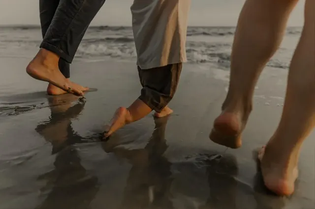 People walking barefoot at the water&rsquo;s edge