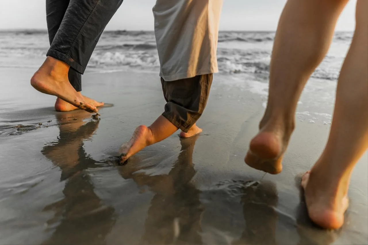 People walking barefoot at the water&rsquo;s edge