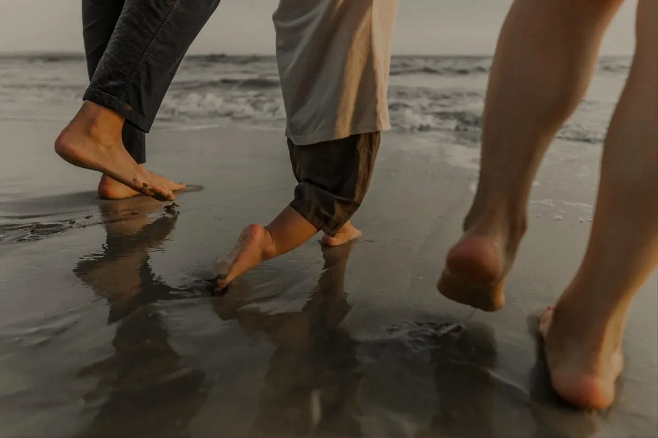 People walking barefoot at the water&rsquo;s edge